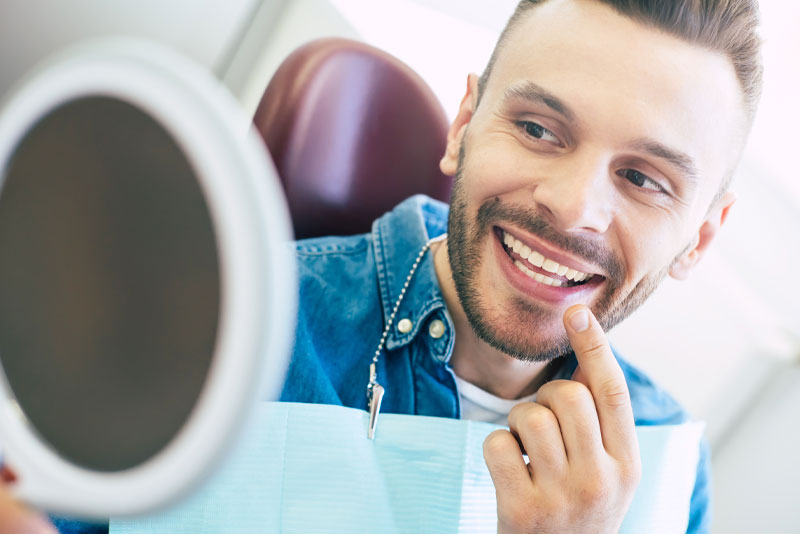 a dental patient smiling at his newly whitened teeth in a hand held mirror after his tooth whitening procedure.