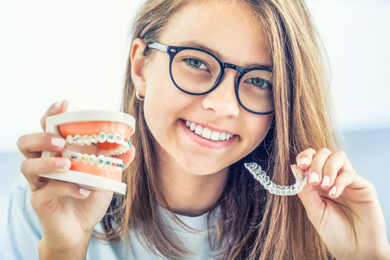 Dental Patient Holding A Dental Model With Braces On In One Hand And Clear Aligners In Her Other Hand