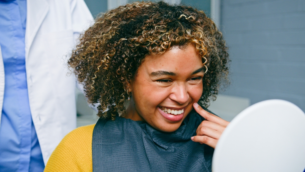 Photo of a senior man smiling genuinely at his dentist, both are happy and in a modern dental office setting. The dentist is pointing to an X-ray on the wall and explaining something to the man. No text on image.
