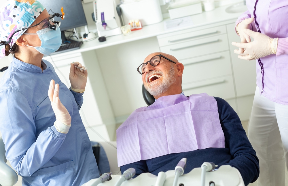 A close-up of a dentist carefully placing a porcelain veneer on a single tooth, with the patient smiling slightly, in a modern dental office setting. No text on image.