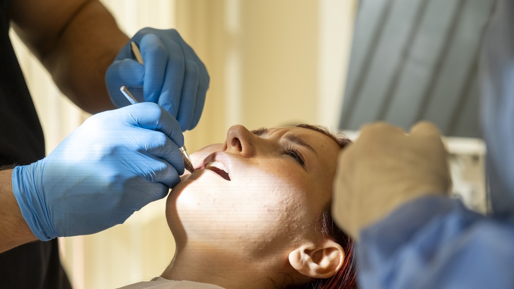 Close up image of a dentist placing a crown on a patient's tooth, with the dentist's hands and dental instruments in focus. No text on image.