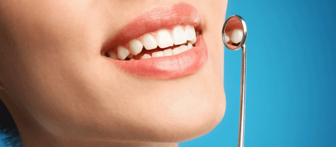 Young woman with mouth mirror on blue background, closeup. Cosmetic dentistry