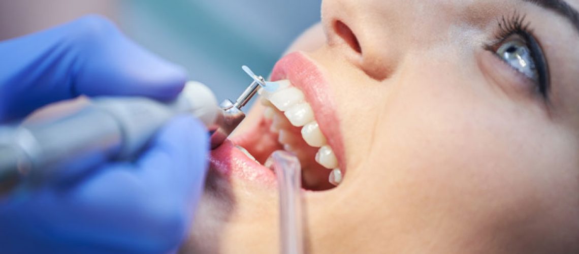 a dental patient undergoing a teeth cleaning procedure, with dental tools in her mouth, for her preventative dentistry needs.