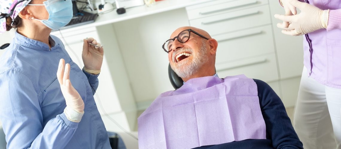 A close-up of a dentist carefully placing a porcelain veneer on a single tooth, with the patient smiling slightly, in a modern dental office setting. No text on image.