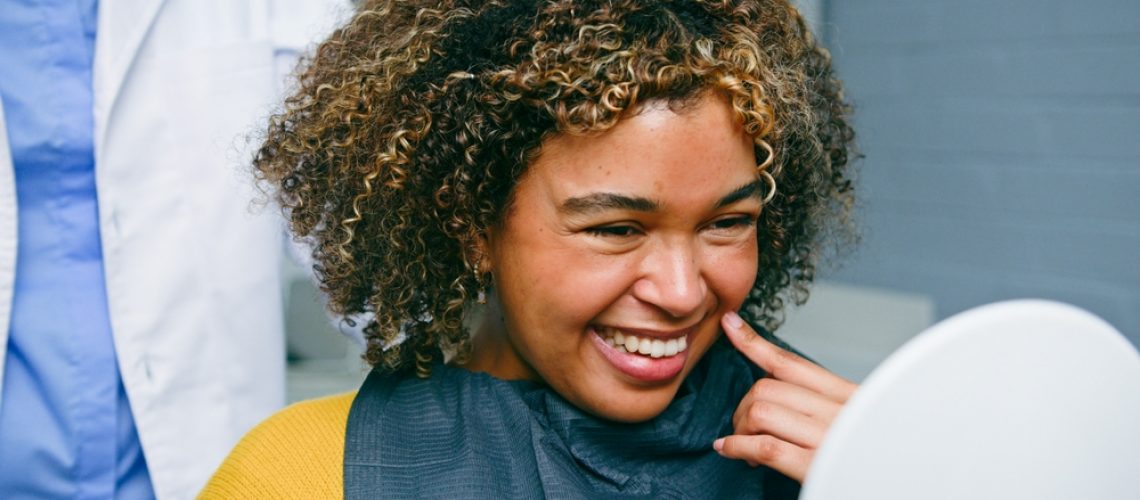 Photo of a senior man smiling genuinely at his dentist, both are happy and in a modern dental office setting. The dentist is pointing to an X-ray on the wall and explaining something to the man. No text on image.
