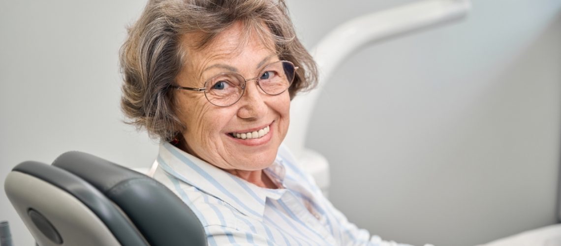 Close-up of a dentist applying a thin porcelain dental veneer to a patient's tooth, showcasing the precision and artistry involved in cosmetic dentistry. The image focuses on the hands of the dentist and the detailed application process, highlighting the natural look and feel of the veneer. No text on image.